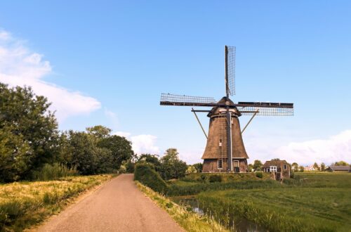 brown windmill on green grass field under blue sky during daytime